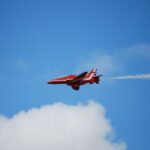 Red jet airplane flying through a cloudy blue sky