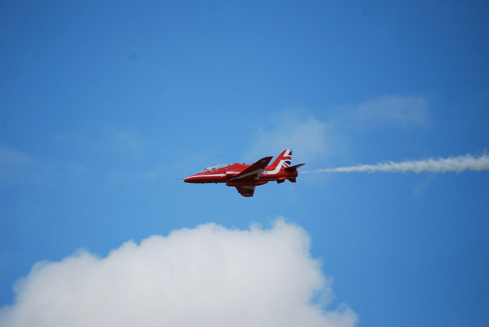 Red jet airplane flying through a cloudy blue sky